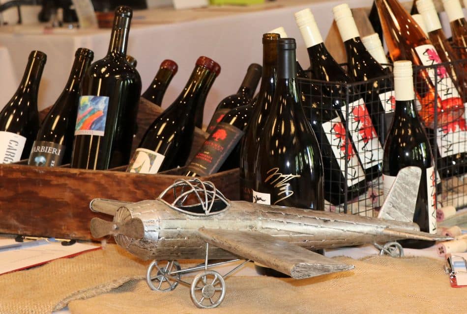 Several bottles of wine in wire and wood baskets next to a metal sculpture of an airplane