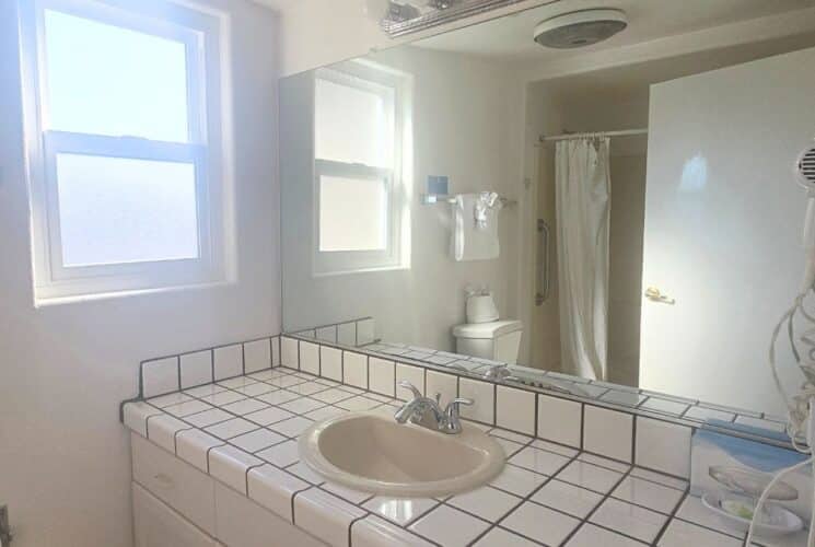 White bathroom with tiled sink vanity, window, shower with curtain