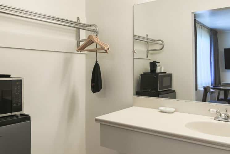 Bathroom with single sink, large mirror, clothing rack with hangers, microwave and mini fridge