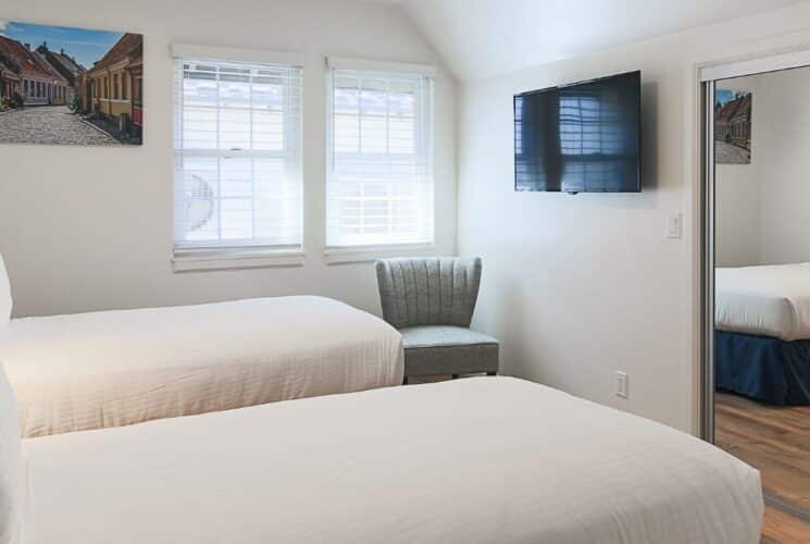 Bedroom with two twin beds, mirrored closet doors, two windows, sitting chair, TV