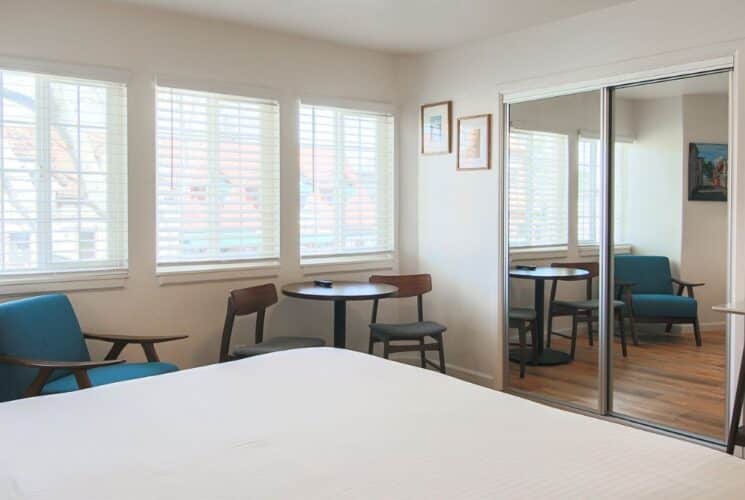 Bedroom with bed, mirrored closet doors, table and three chairs, TV over buffet table and three windows