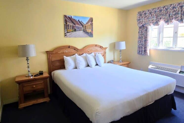 Bedroom with queen bed in white sheets, large window with floral valence, side tables with lamps