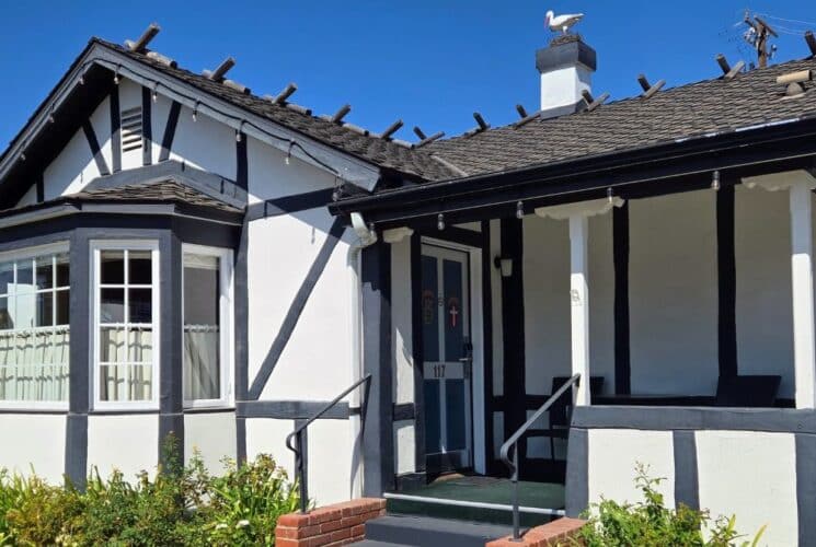 A white cottage with brown trim with front steps with green bushes