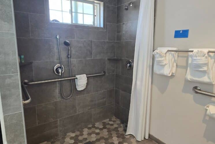 Bathroom with large walk in tiled shower, grab bars, shelving with towels