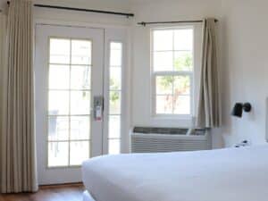 Bright bedroom with king bed, French door, beige curtains and colorful artwork