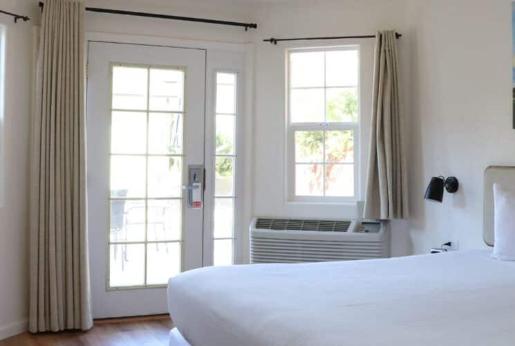 Bright bedroom with king bed, French door, beige curtains and colorful artwork