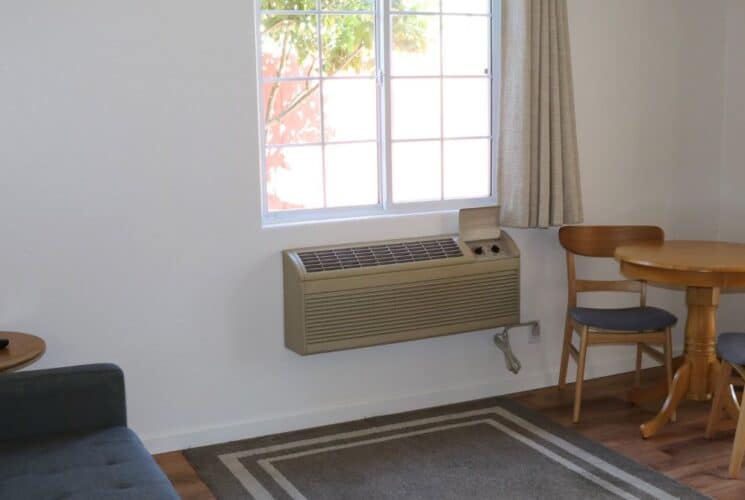 Sitting area with couch, table and two chairs, rug and window with beige curtains