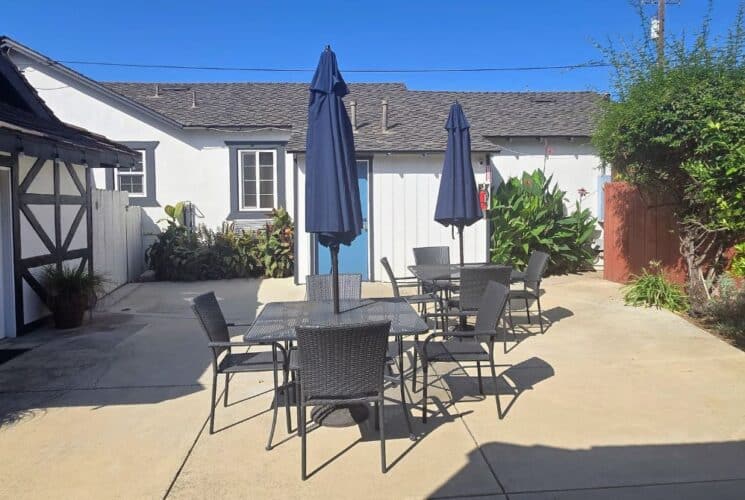 Outside patio with tables and chairs and blue patio umbrellas next to white buildings with black trim