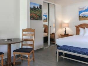 Bedroom with bed with wood headboard, mirrored closet, table with two chairs and colorful artwork