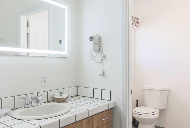 Spacious white bathroom with tiled sink vanity, lit mirror, toilet closet