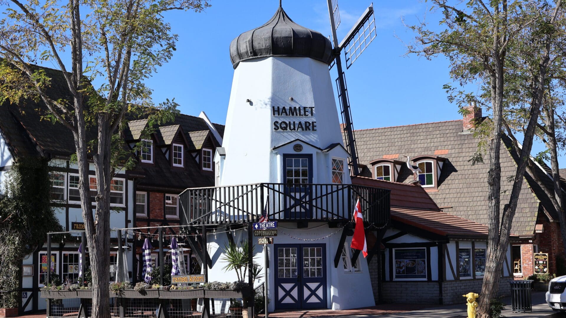 A tall white windmill building at the corner of a shopping district