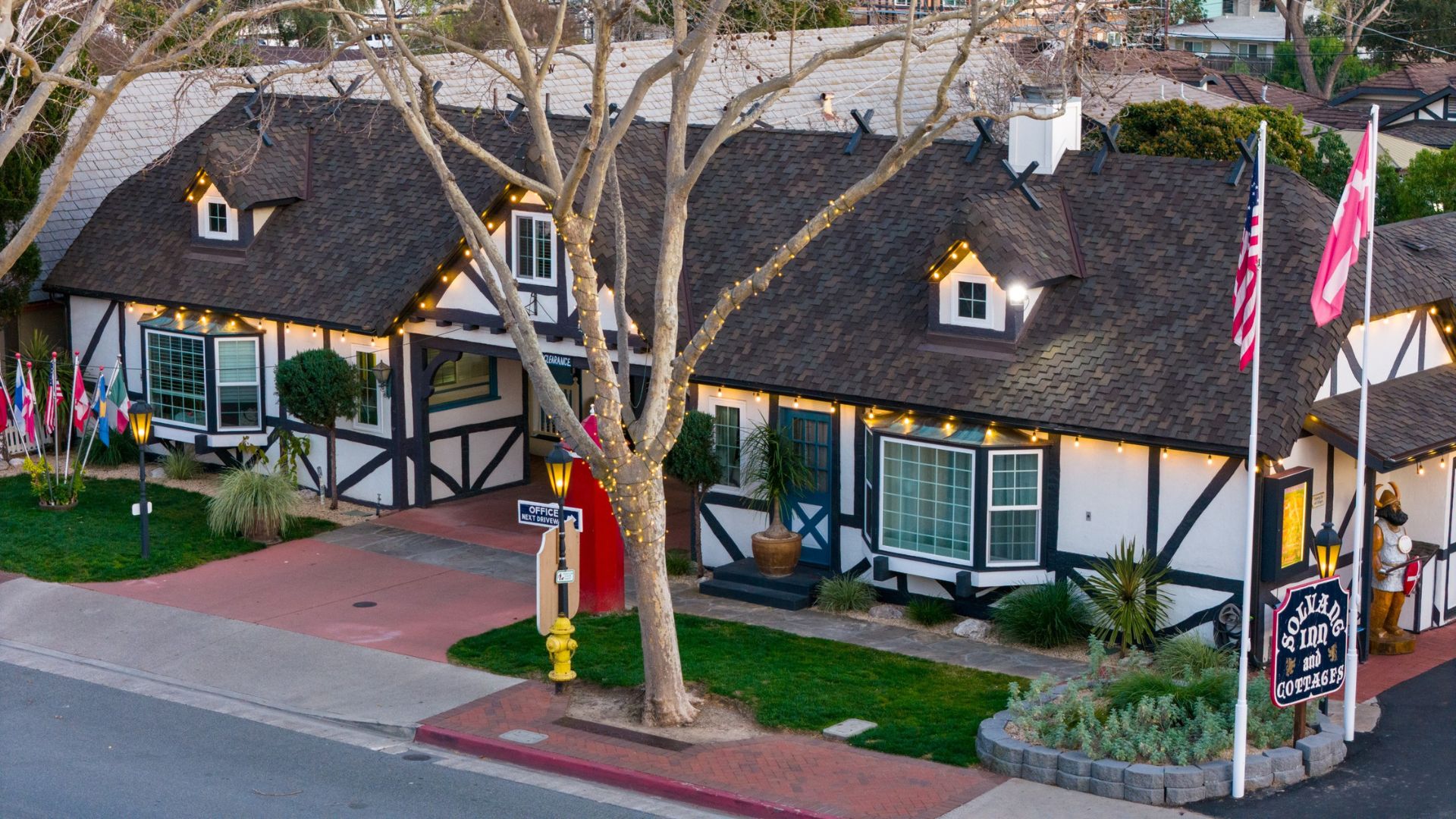 An expansive white and brown inn building with white Christmas lghts, large tree sign and flags in the front yard