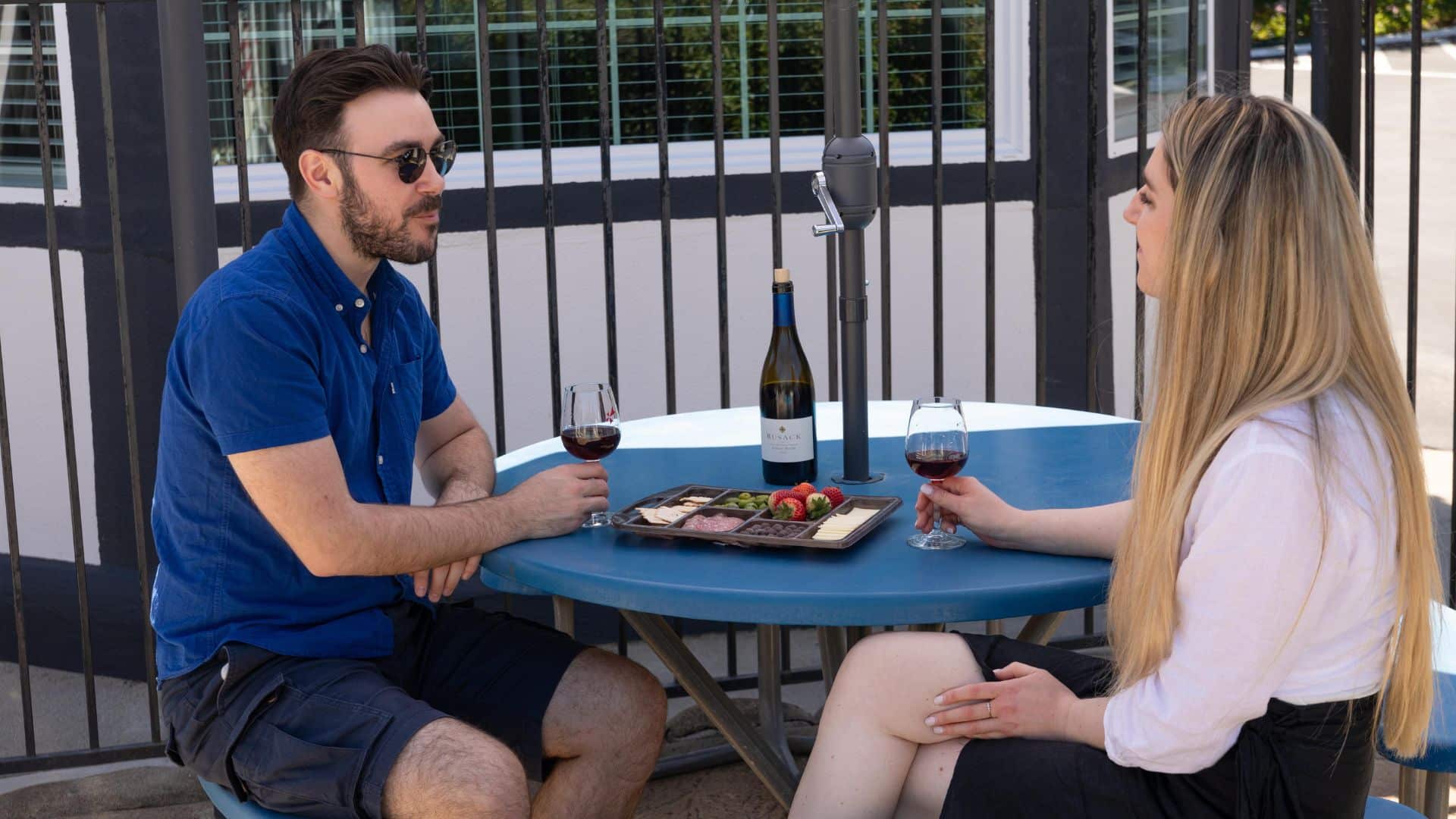 A man in a blue shirt with a woman in a white blouse sitting at an outdoor patio table enjoying wine and charcuterie